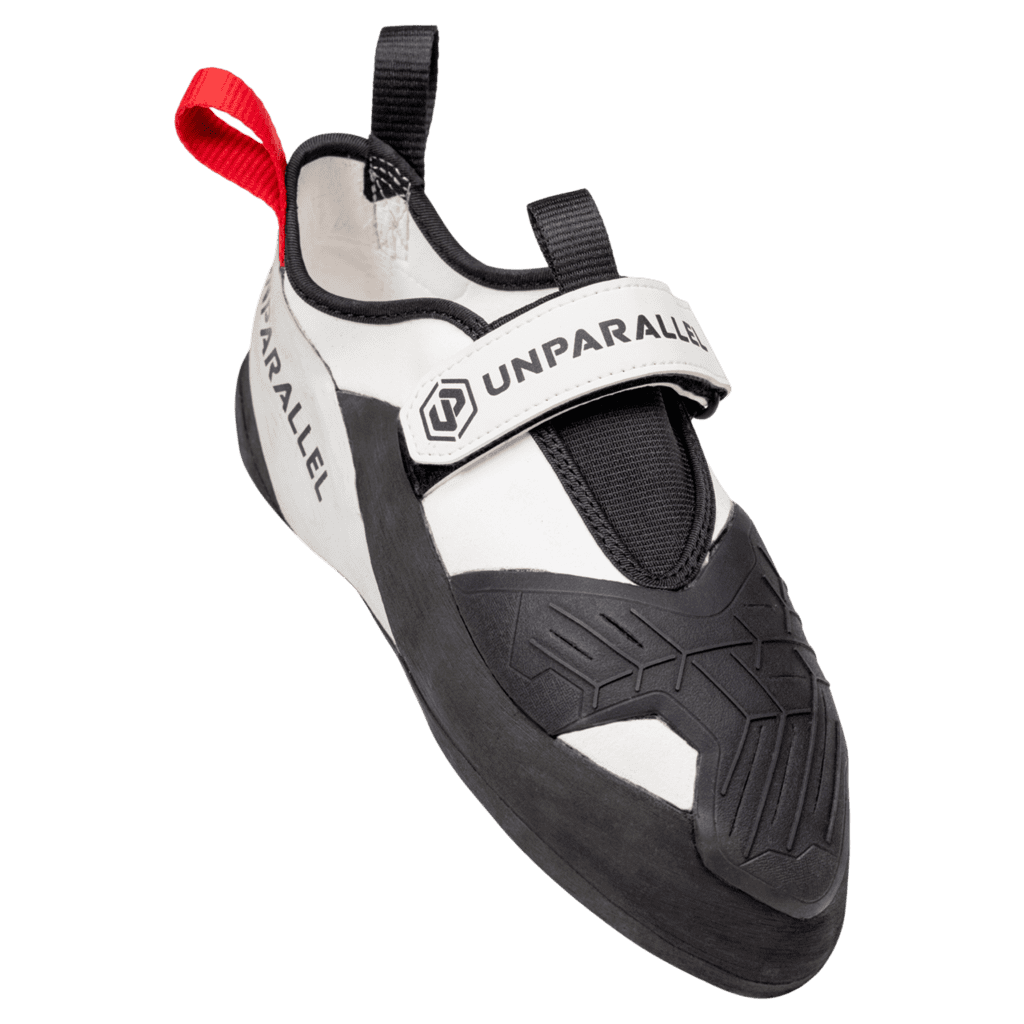White and black climbing shoe with a Velcro strap and red pull tab at the heel, branded Unparallel on the strap and side.